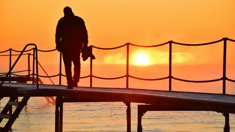 En person står ved vandet og kigger på solnedgangen